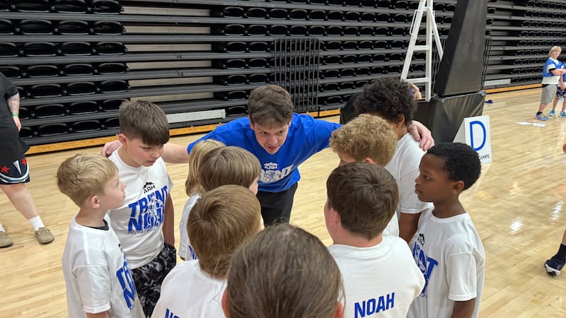Trent Noah huddles with group of campers at basketball camp.